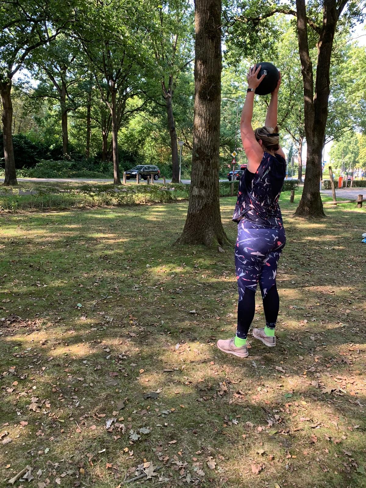 Trainster tilt een kettlebell boven het hoofd in het park